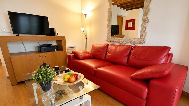 Ein modernes Wohnzimmer mit einem roten Ledersofa, einem Glastisch mit Früchten, einem Flachbildfernseher und einer Holzkabine.