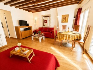 A cozy living room with a red sofa, a television, a wooden cabinet, and a dining area with a table set for two. - Le Loft Boissy (Paris)