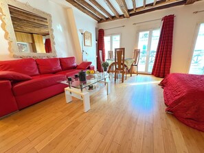 A cozy living room with a red sofa, a glass coffee table, and a dining area with wooden chairs and a table. - Le Loft Boissy (Paris)