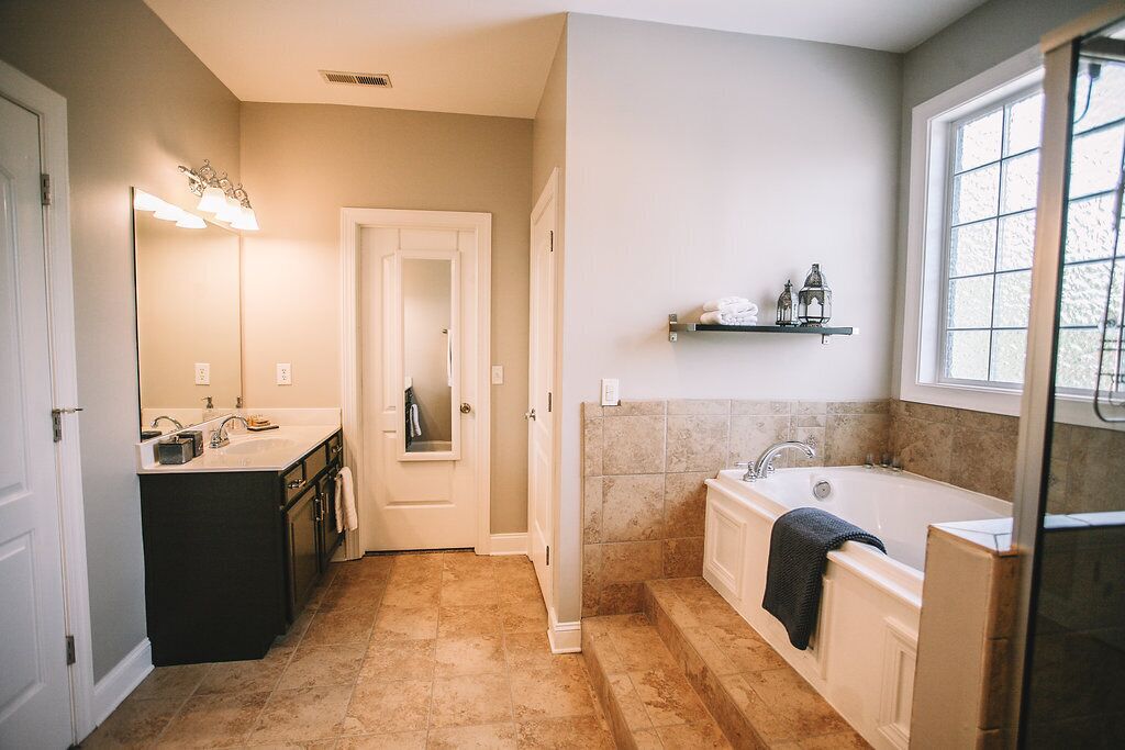 Un bagno con vasca, lavabo e specchio. Una finestra offre luce naturale e uno scaffale con articoli da toilette.