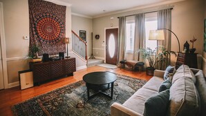 Ein Wohnzimmer mit einer Couch, einem Couchtisch, einem Wandteppich, einer Treppe und einer Tür mit Vorhängen.