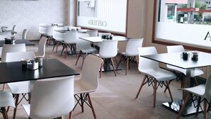 A modern conference room with white tables and chairs, a large window with a view of buildings, and a plant in the corner. - Hotel Reigosa (Ponte Caldelas)