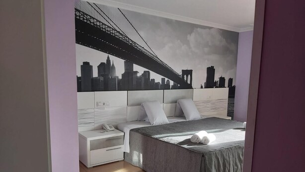 A bedroom with a bed, nightstands, and a cityscape mural on the wall. - Hotel Reigosa (Ponte Caldelas)