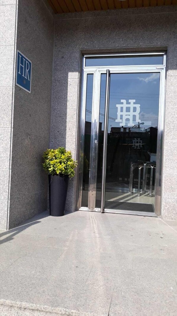 A building entrance with a glass door, a potted plant, and a sign with 'HR' on the wall. - Hotel Reigosa (Ponte Caldelas)