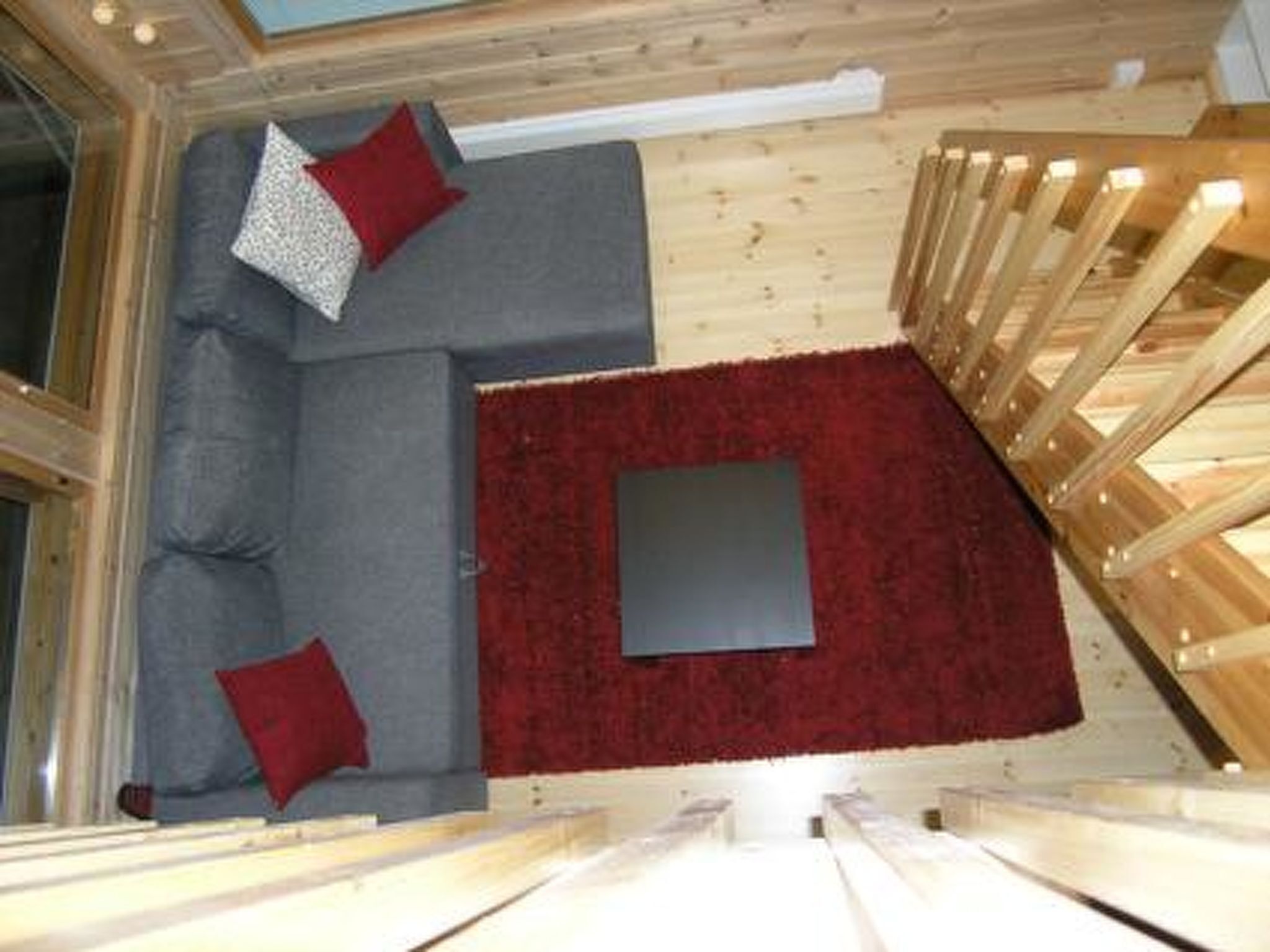 A high-ceilinged room with a grey sofa, red cushions, and a red rug.