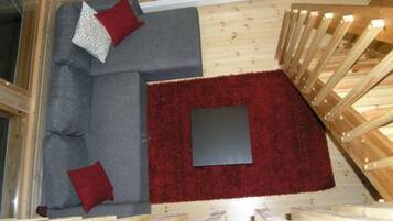 A high-ceilinged room with a grey sofa, red cushions, and a red rug.