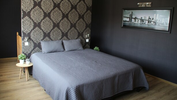 A bedroom with a large bed, a small side table with a plant, a framed picture on the wall, and a patterned wallpaper. - Spacious vacation home with covered patio and sun terrace (Middelkerke)