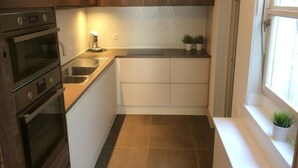 A compact kitchen with dark wooden cabinets, a stainless steel sink, and a tiled backsplash. - Spacious vacation home with covered patio and sun terrace (Middelkerke)