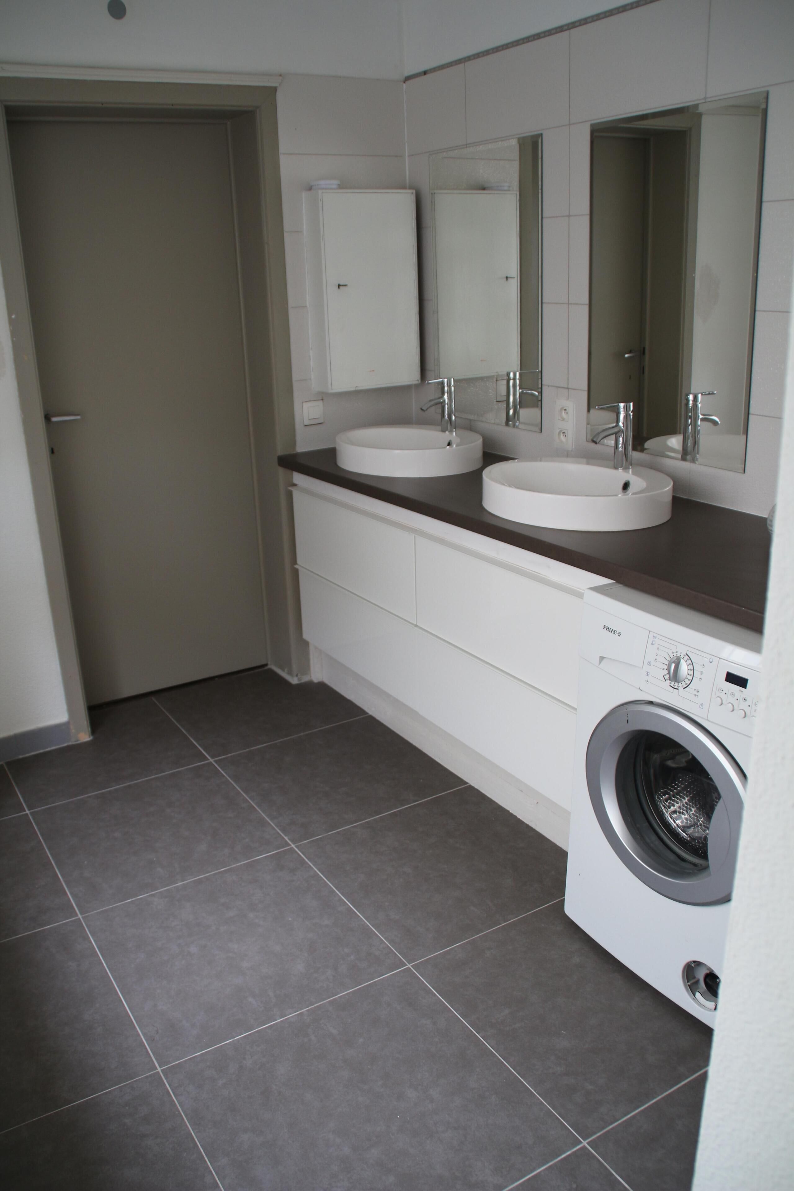 Un baño moderno con dos lavamanos, un espejo y una lavadora.