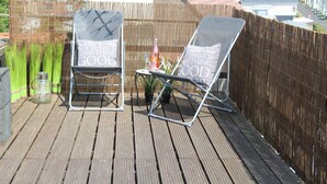Two lounge chairs with a table and a bottle of water on a wooden deck with a bamboo fence. - Spacious vacation home with covered patio and sun terrace (Middelkerke)