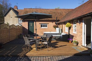 A patio with a table and chairs, a wooden fence, and a brick building with a green door. - West Mead Cottage (Wirral)