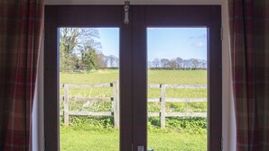 A view through a wooden door with a metal latch, leading to a grassy field and a wooden fence. - West Mead Cottage (Wirral)