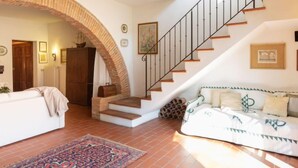 Un salon avec un canapé blanc, un tapis à motifs, un escalier en bois et une arche en briques.