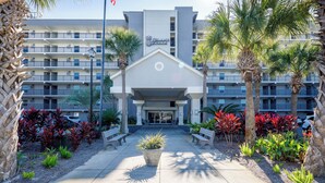 A hotel entrance with a central pathway, palm trees, and benches.