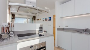 Ett modernt kök med vita skåp, en inbyggd ugn, en rostfri köksfläkt och ett stort fönster.