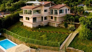 A multi-story house with a swimming pool, a covered patio, and a lush garden.
