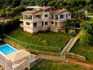 Une maison à plusieurs étages dotée d’une piscine, d’un patio couvert et d’un jardin luxuriant.