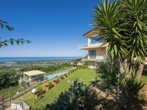 Ein zweistöckiges Haus mit Pool, umgeben von einem gepflegten Garten und Blick aufs Meer.