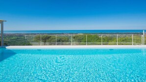 A clear blue pool with a view of the ocean and greenery in the background.
