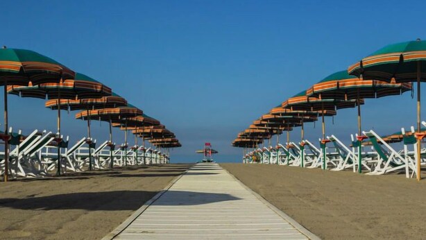 A beach with rows of striped umbrellas and white lounge chairs.