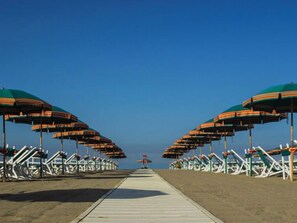 Ein Strand mit Reihen von gestreiften Sonnenschirmen und weißen Liegestühlen.