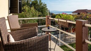 Een balkon met rieten meubilair, een kleine ronde tafel en uitzicht op zee en bergen.