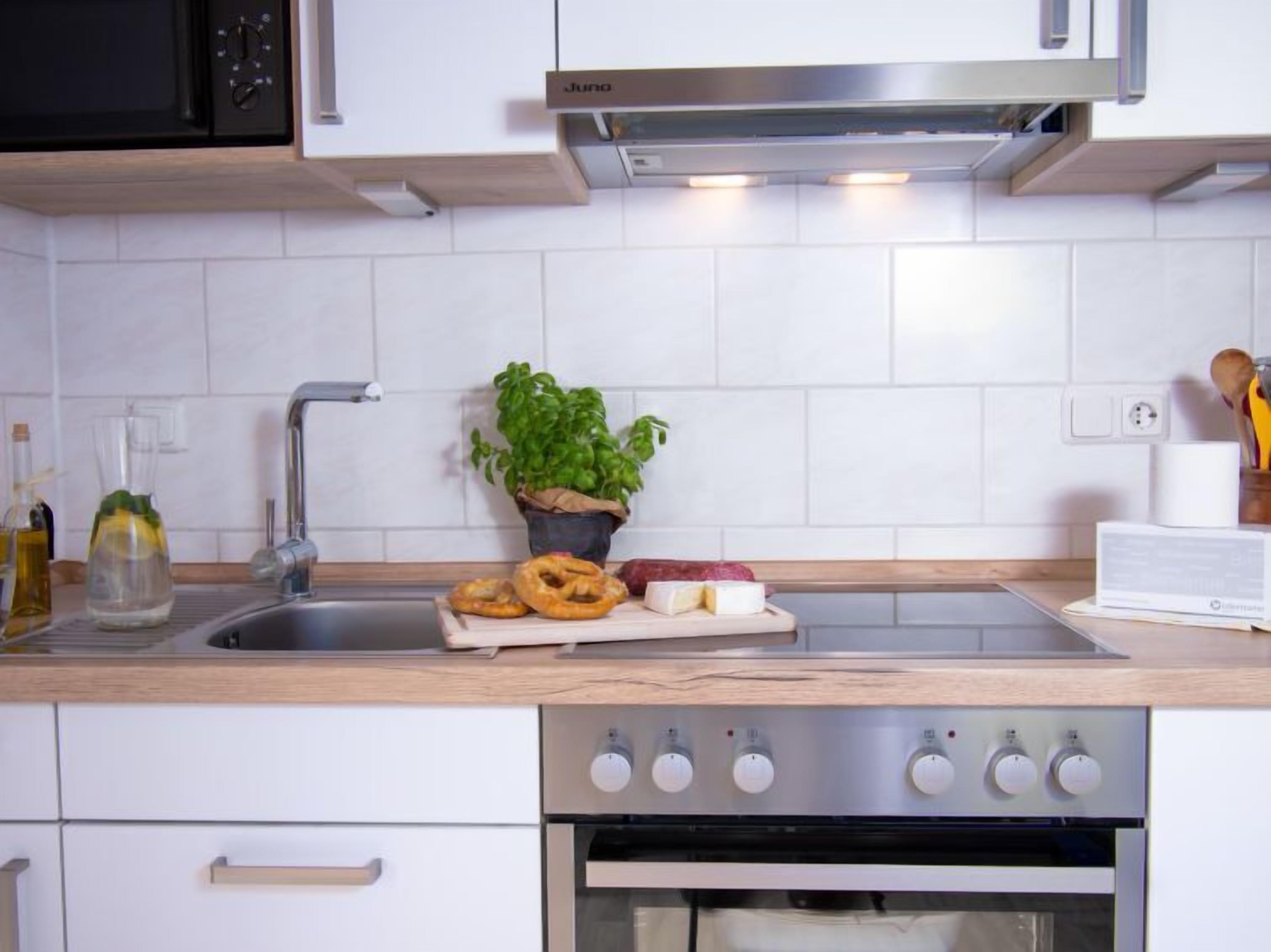 A modern kitchen with white cabinets, a stainless steel sink, a built-in oven, and a potted plant.