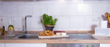 A modern kitchen with white cabinets, a stainless steel sink, a built-in oven, and a potted plant.