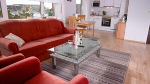 A modern living room with a red sofa, a glass coffee table, and a view of the kitchen. - Lachmöwe by Interhome (Norddeich)