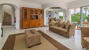 A spacious living area with a sofa, ottoman, and wooden cabinet. A staircase and a dining area are visible in the background. - Arribas Villa by Interhome (Guia)