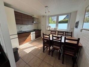 A compact kitchen with a dining area, a window with a view, and a trash bin.