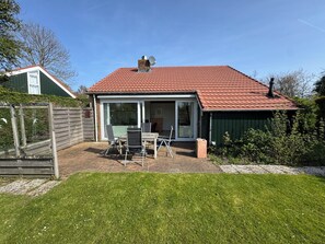 A house with a red-tiled roof, a glass door leading to a patio, and a small table with chairs. - Detached 6 persons holiday home, completely fenced garden in holidaypark Zomerdorp (Brouwershaven)
