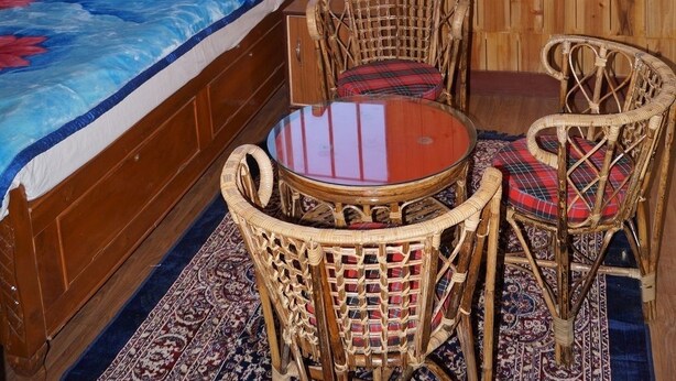 Ein Zimmer mit Holzwänden, einem Bett, zwei Korbstühlen, einem kleinen Tisch und einem Fenster mit Gitterstäben.