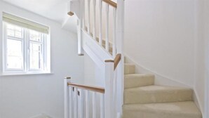 Una escalera con barandillas blancas y peldaños alfombrados en tono beige.
