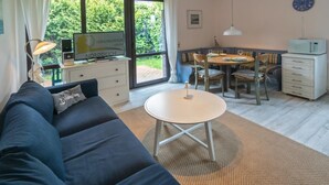 Un salon moderne avec un canapé bleu foncé, une table ronde blanche et un coin repas comprenant une table et des chaises en bois.