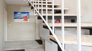 Un escalier moderne avec des marches en bois et des rampes blanches, menant à un palier où se trouvent un tapis noir et un extincteur rouge.