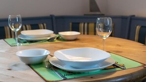Une table à manger avec des bols blancs et des verres à vin, disposés sur un set de table vert orné d’un dessous de verre sur le thème de la marine.