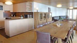 A modern kitchen with wooden cabinets, a central island, and a dining area with a long table and chairs. - Apartment Gloria by Interhome (Mürren)