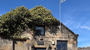 Il s’agit d’un bâtiment en pierre sur lequel on peut lire l’inscription « Abbey House ». Un grand arbre se trouve devant, ainsi qu’une antenne parabolique et une fenêtre avec des volets.