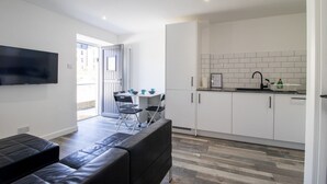 Un appartement moderne comprenant un espace de vie, une table à manger, une cuisine avec des meubles blancs et un téléviseur à écran plat fixé au mur.