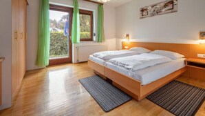 Ein Schlafzimmer mit einem großen Bett, einem Holzschrank, einem Heizkörper und einem Fenster mit grünen Vorhängen.