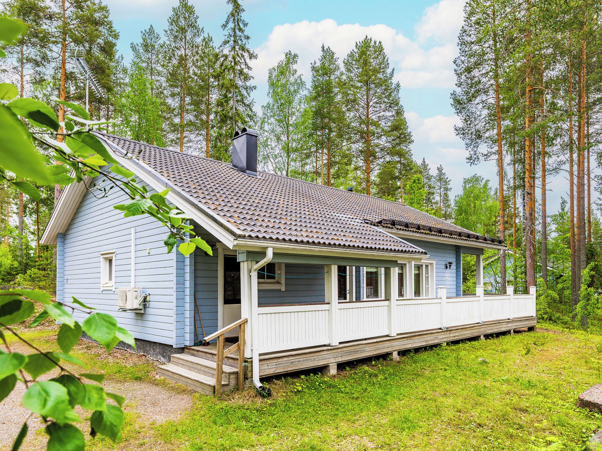 Sininen mökki, jossa on kuisti, ja sen ympärillä on puita.