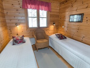Une cabine comprenant deux lits, une chaise, une fenêtre avec des rideaux et des lampes fixées au mur.