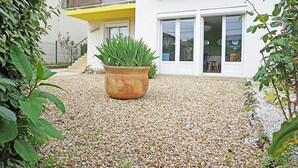 A modern house with a gravel driveway, a large potted plant, and a balcony with yellow trim.