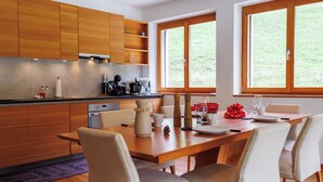 Een moderne keuken met houten kastjes, een eettafel met stoelen en grote ramen met uitzicht op de omgeving.