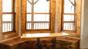A wooden interior with a bench seating area, large windows, and a chandelier.