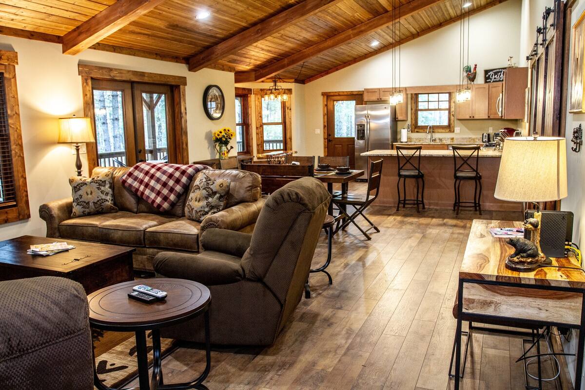 Una sala de estar acogedora con un sofá, sillones y una mesa de centro. Hay un comedor con una mesa y sillas, y una cocina con un refrigerador y armarios.