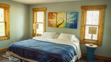 A bedroom with a bed, a painting, two windows with blinds, and a ceiling fan.