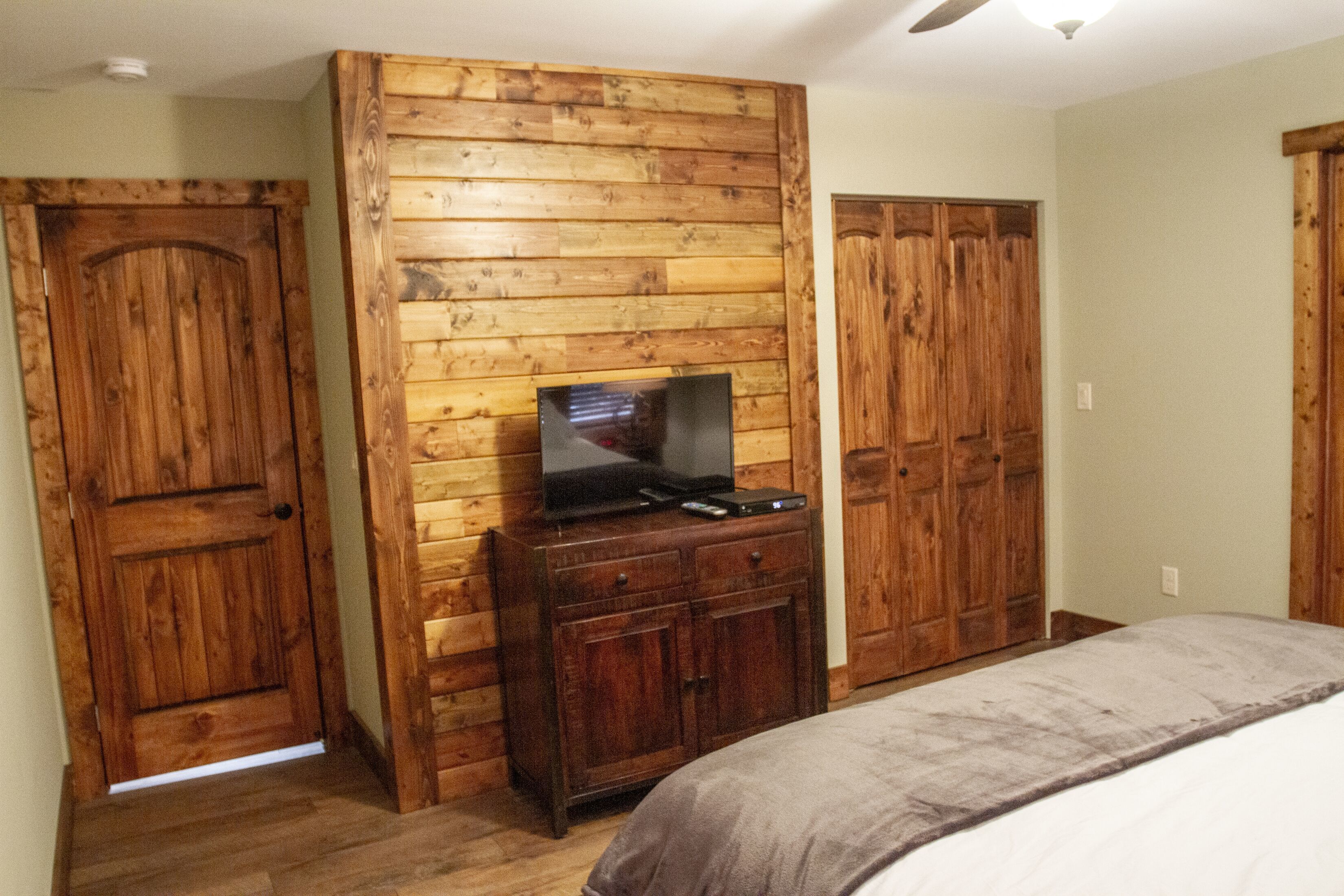 A bedroom with wooden paneling, a bed, a TV on a wooden cabinet, and a wardrobe.