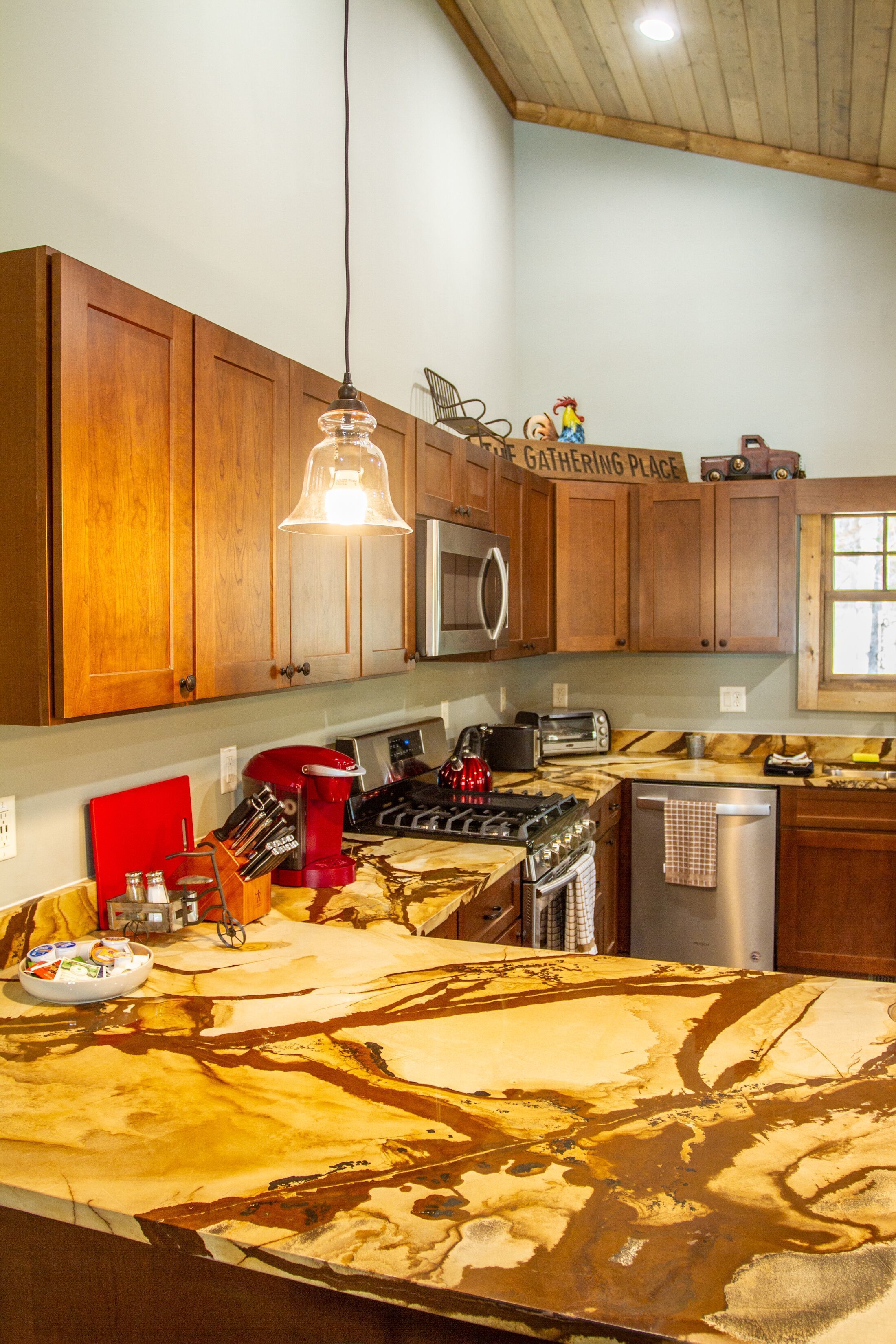 A kitchen with wooden cabinets, a gas stove, a microwave, and a red kettle.